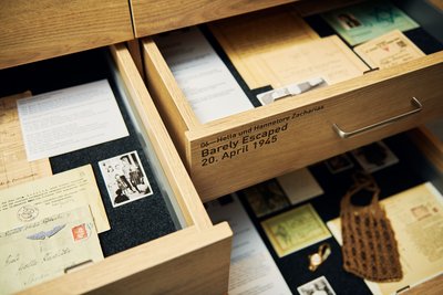 Blick in zwei geöffnete Schubladen mit Unterlagen, Briefen und Fotos. Auf einer Schublade ist zu lesen: Hella und Hannelore Zacharias. Barely Escaped, 20. April 1945