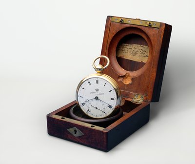 Der Humboldt-Chronometer ist eine Taschenuhr mit weißem Ziffernblatt. Die Uhr wird stehend in ihrer Holzschatulle gezeigt.