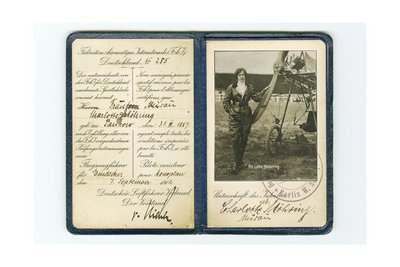 Flugzeugführerschein, aufgeklappt. Die personenbezogenen Daten wurden mit schwarzer Tinte handschriftlich auf der linken Seite eingetragen. Die rechte Seite enthält ein Schwarzweiß-Foto einer Frau vor einem Flugzeug. Unterhalb des Fotos befindet sich die Unterschrift von Frau Charlotte Möhring und ein Stempel.