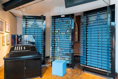 Die drei Speicherschränke des Nachbaus des Zuse-Computers Z3 sind jeweils 2,20 Meter hoch und 1,20 Meter breit und mit insgesamt 1.600 blauen Schaltrelais bestückt. Links im Vordergrund steht die schwarze Bedienkonsole mit vielen Zahlen- und Funktionstasten.