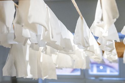 Eine Reihe weißer Papierbögen hängt zum Trocknen auf einem Holzgestell.