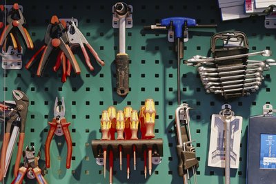 Werkzeuge wie Hammer und Zangen hängen an einer grünen Wand.