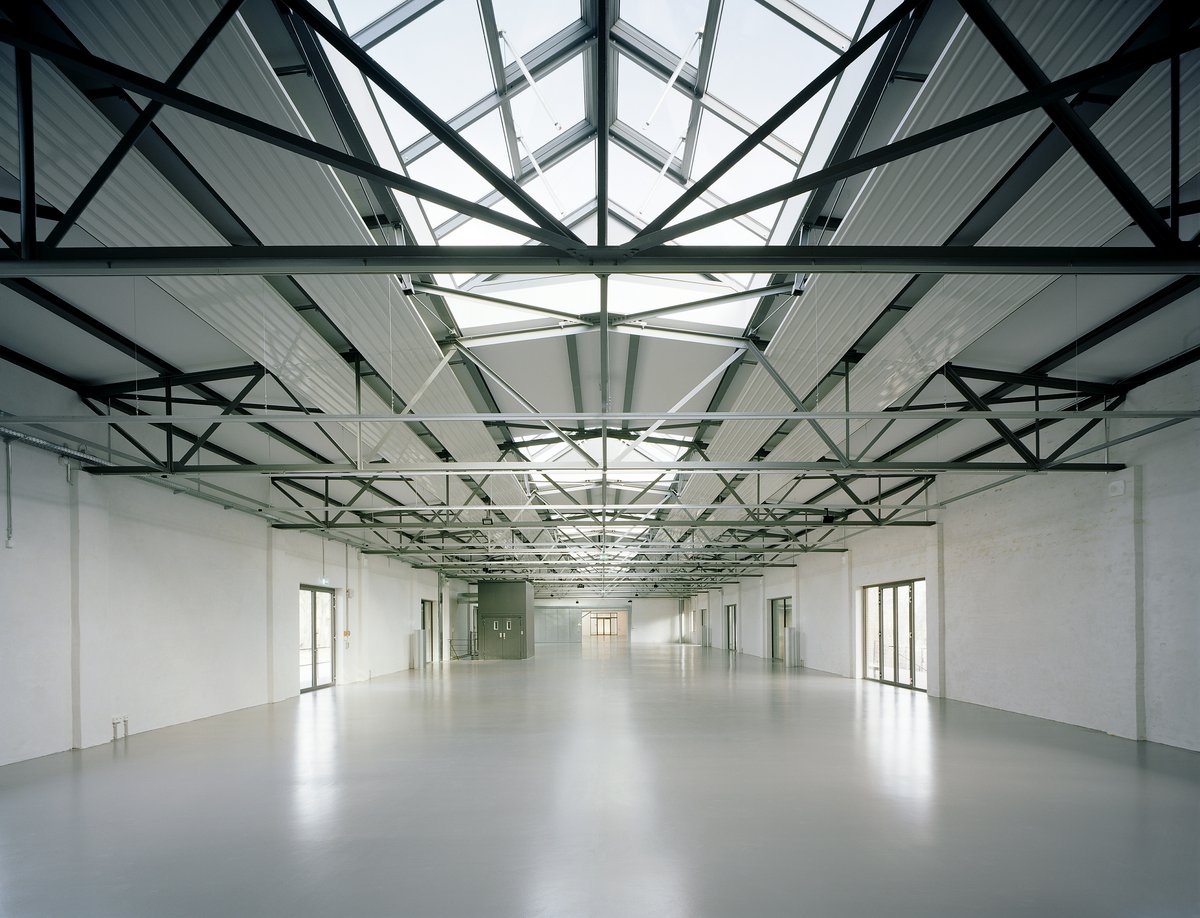 Blick in eine Lagerhalle, die offensichtlich neu restauriert wurde: Die Böden und Wände glänzen weiß, die Stahlkonstruktion der Decken geben den Blick auf Glasgauben frei.