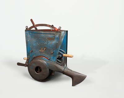 Das Stäubegerät ist aus Metall, seine Seitenteile sind blau. Es ist oben offen und hat einen roten Tragegriff. An der rechten Seite sitzt eine Handkurbel mit hölzernem Griff. An der Vorderseite befindet sich ein Rohr mit einer am Auslass verbreiterten Tülle, durch die das Insektenpulver verstreut wurde. 