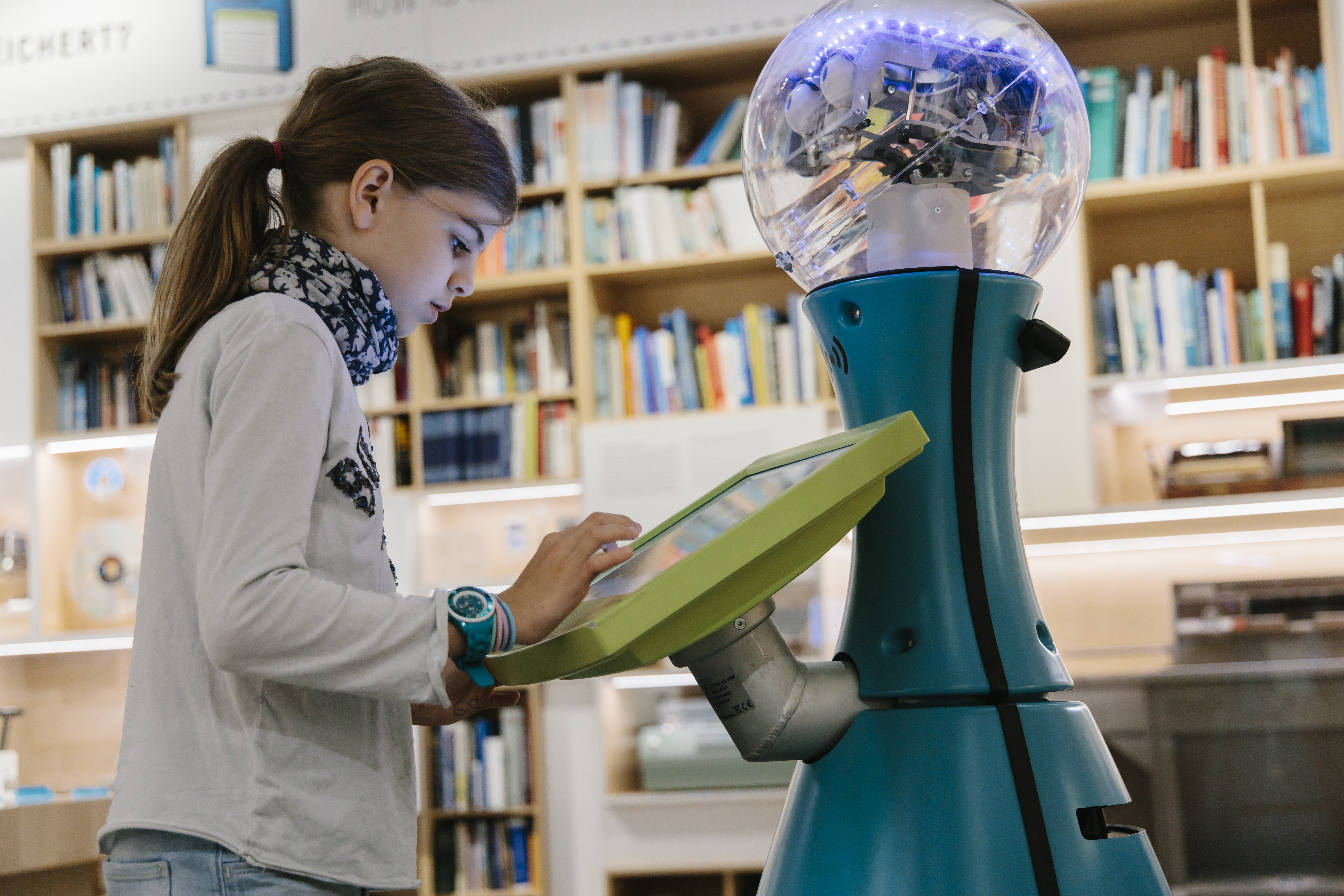 Ein Mädchen tippt etwas auf dem Display einen humanoiden Roboters.
