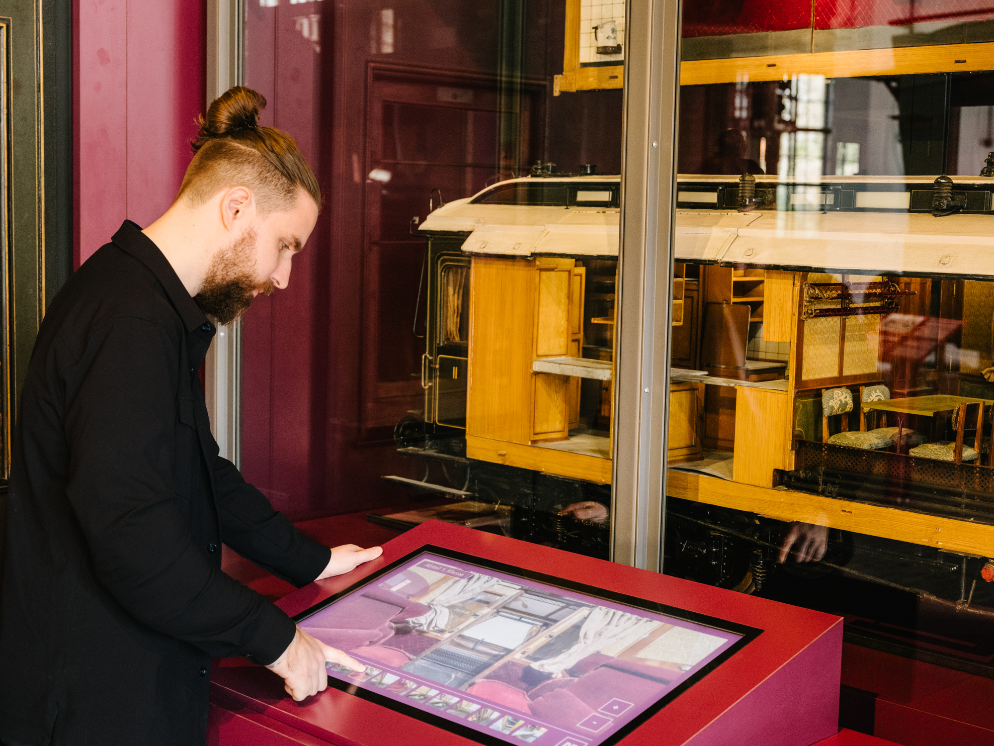 Ein Mann steht vor einer Vitrine mit Eisenbahnmodellen. Vor sich ein Bildschirm, auf dem er herumtippt.