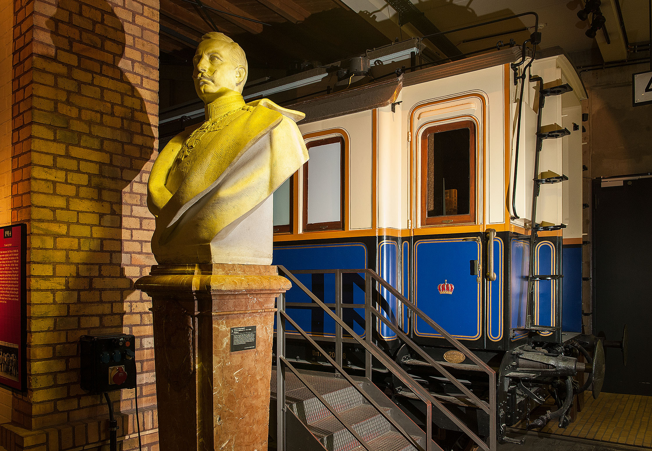 Büste von Kaiser Wilhelm II. vor einem blau-weißen Eisenbahnwagen