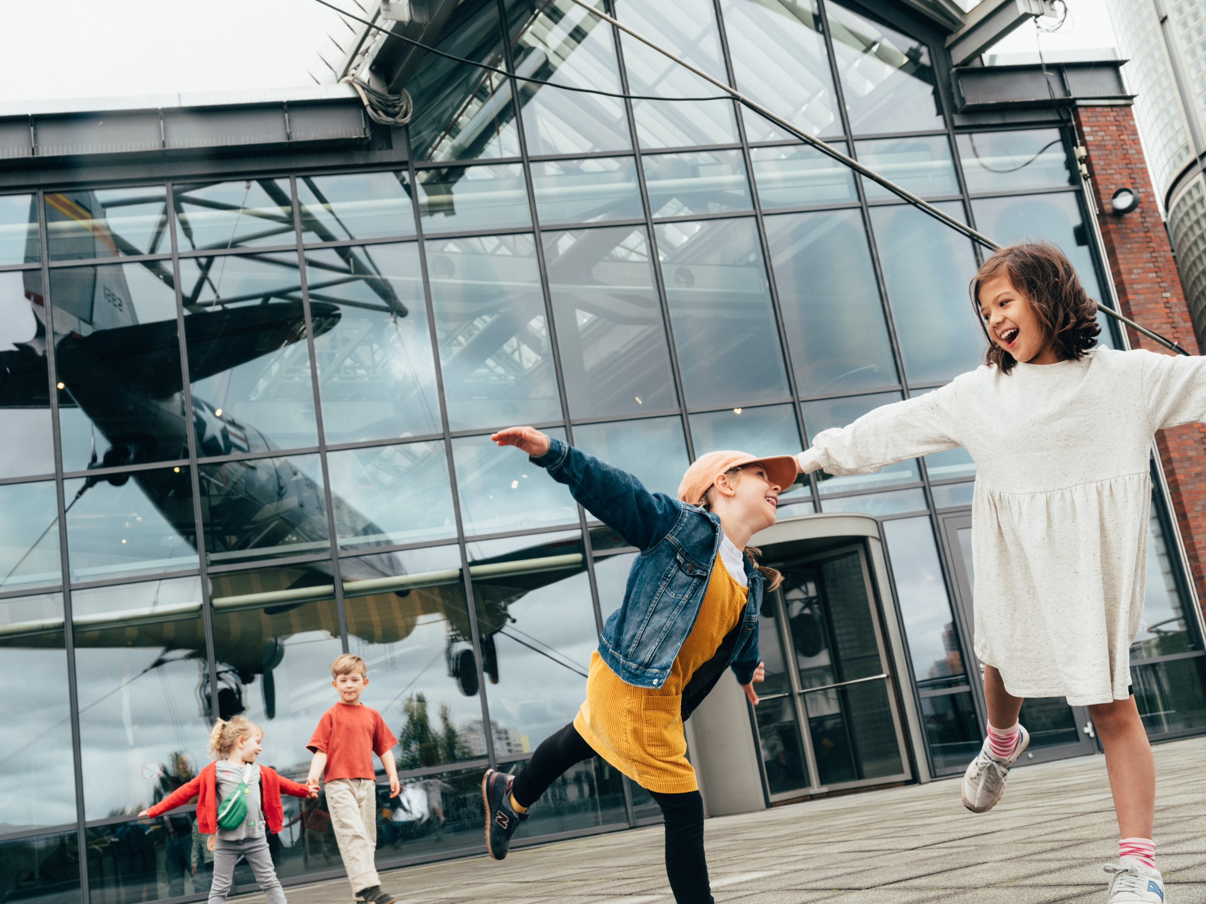 Vier Kinder auf der Terrasse des Museums, in der Glasfront spiegelt sich der Rosinenbomber, der dort aufgehängt ist.