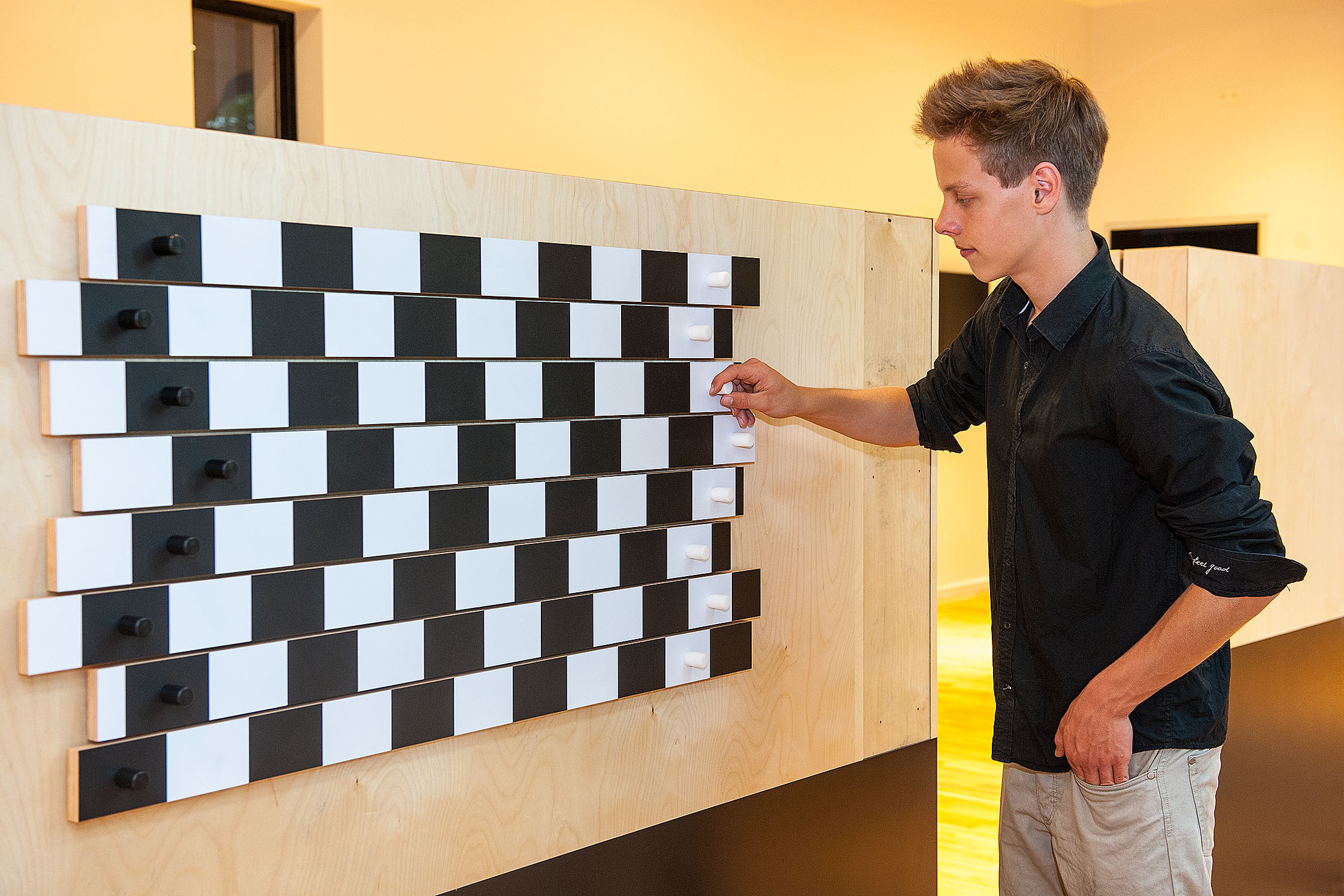Ein Mann bedient ein Experiment an einer Wand: Schwarz-weiß gestreifte Leisten sind gegeneinander verschoben. Sie erscheinen schief.